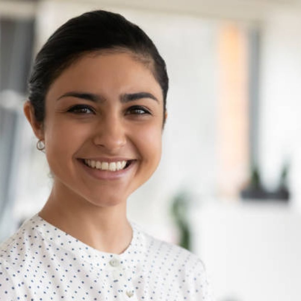 Head shot portrait of confident successful smiling Indian businesswoman standing in office, happy entrepreneur employee executive looking at camera, posing for corporate photo, profile picture
